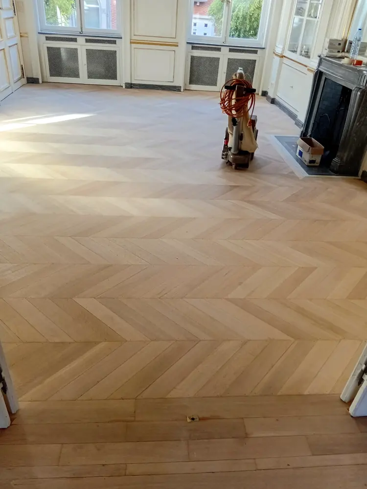 Parquet à chevrons poncé avec une ponceuse près d’une cheminée